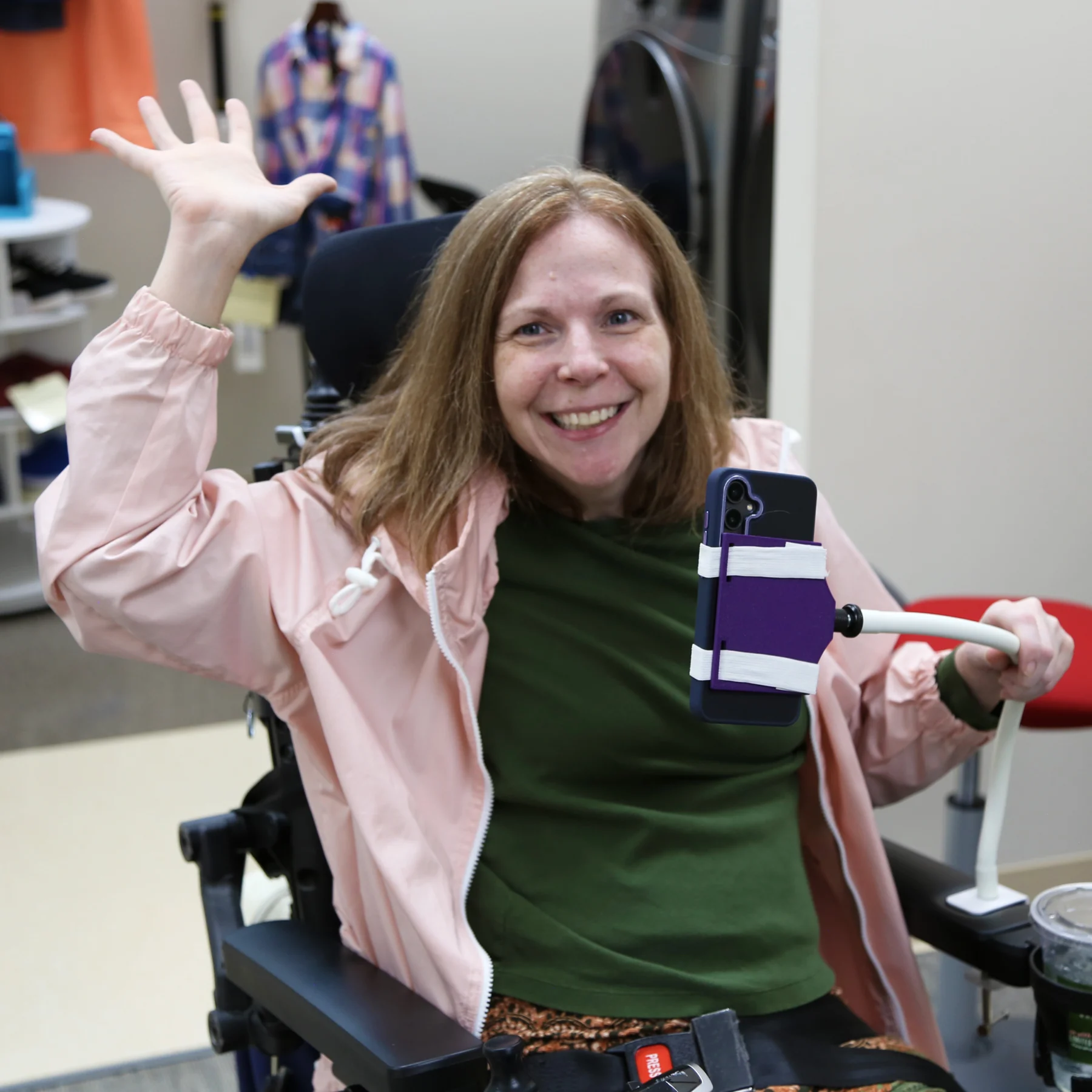 Meredith with her phone attachment on her Quantum chair waving at the camera