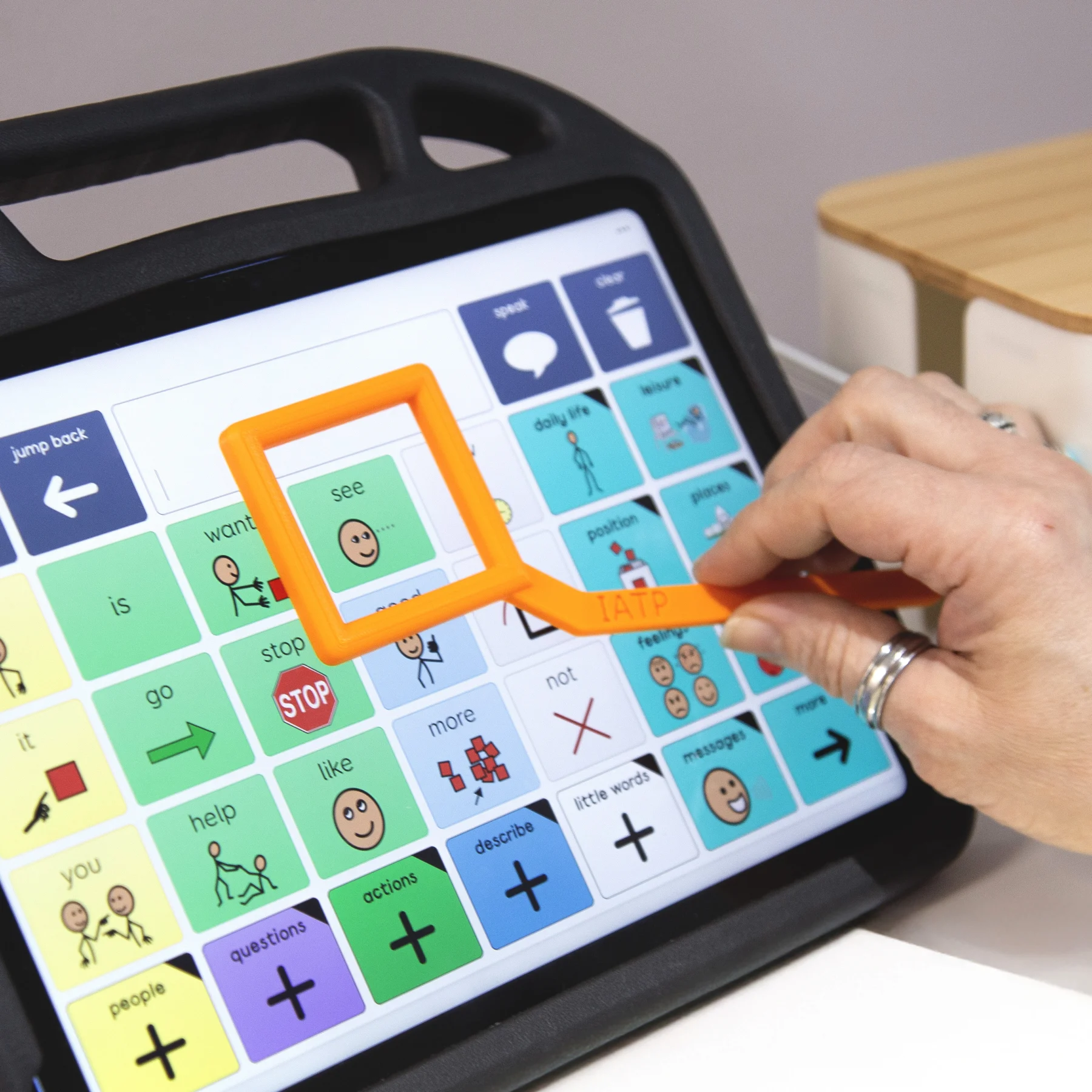 Someone holding the visual prompting device to prompt the 'see' button on an AAC device