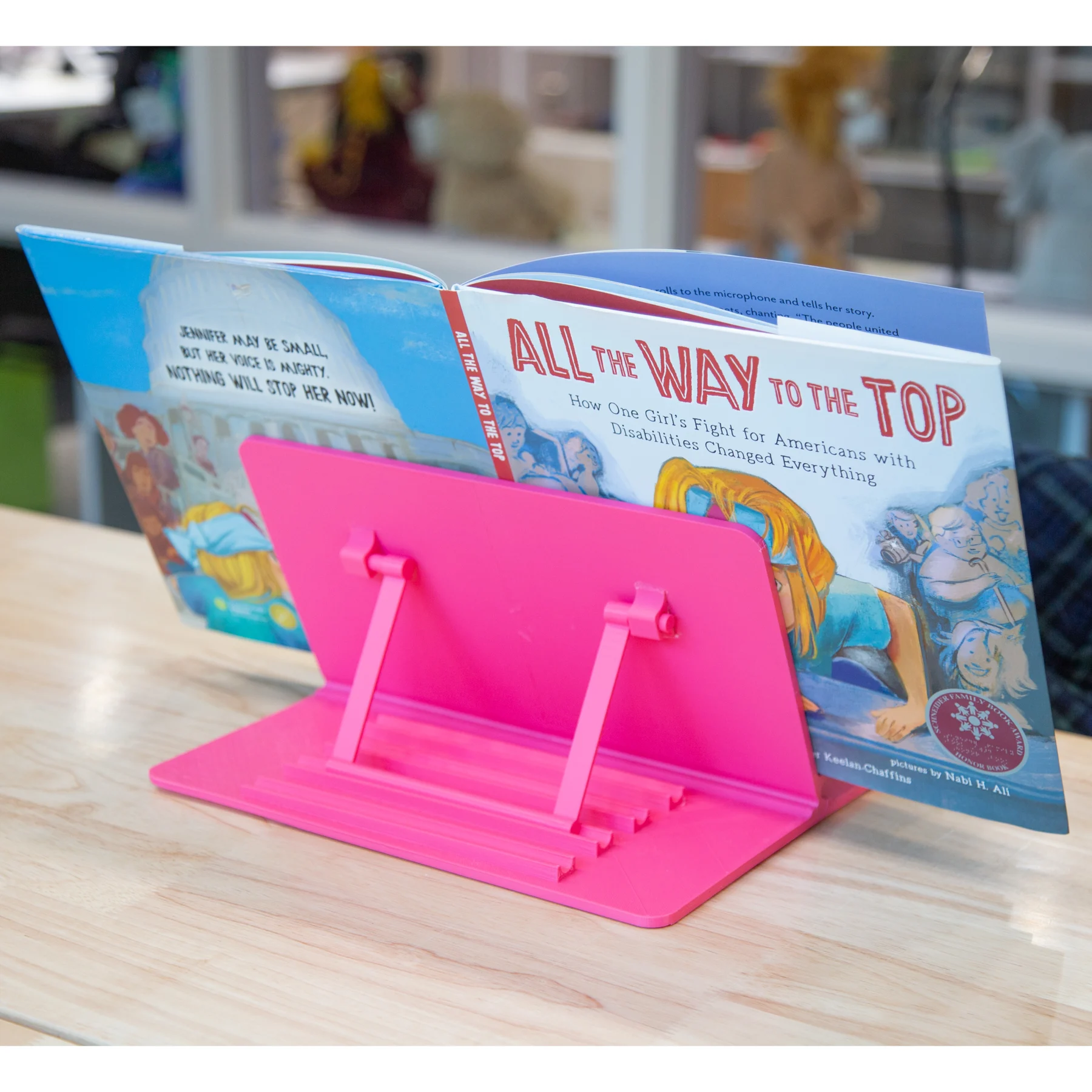 Showing backside of the Adjustable Tablet Stand resting on a table holding the book All the way to the top by Annette Bay Pimentel