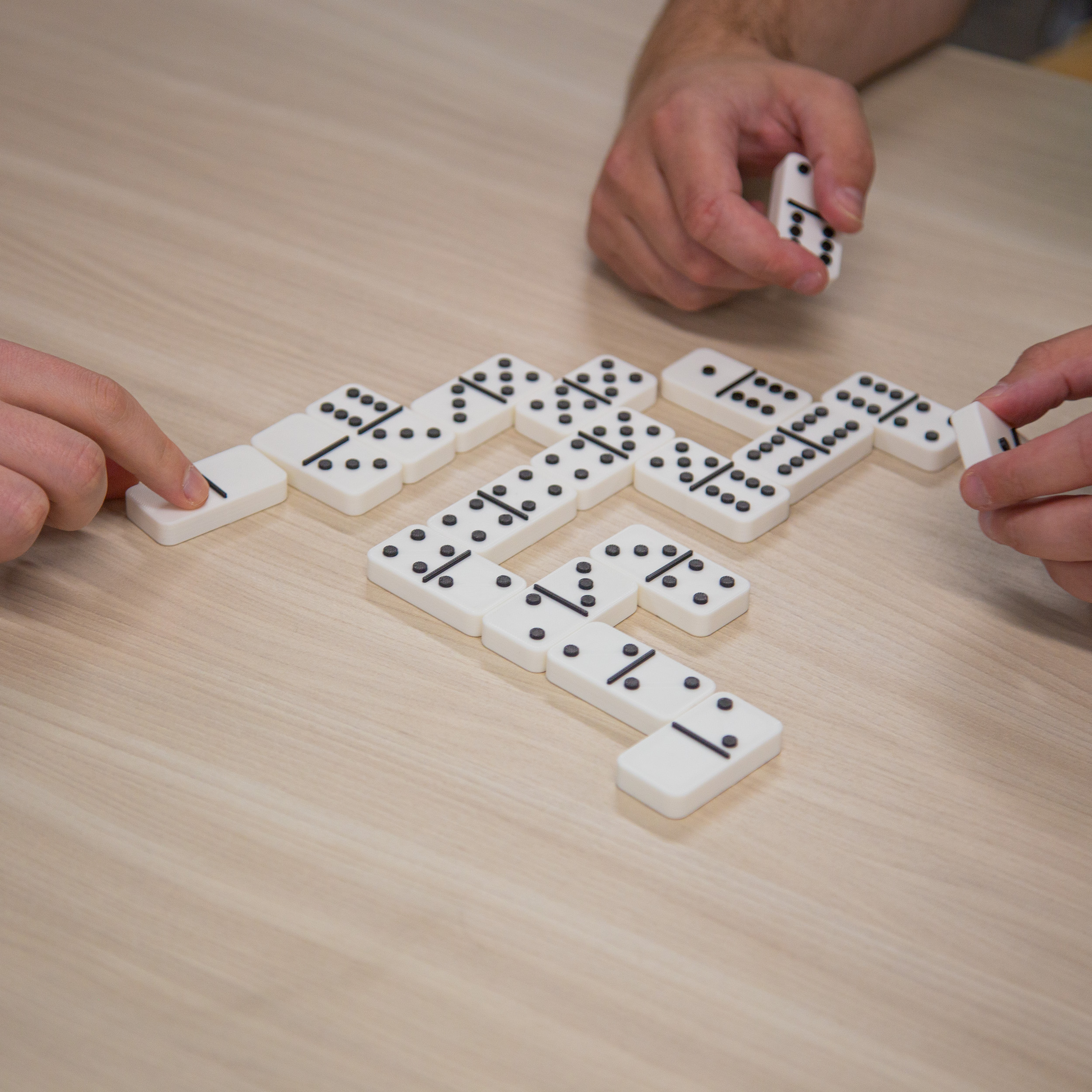 Two men playing dominos with tactile dominos, one of the men are feeling the tile to see how many dots are there